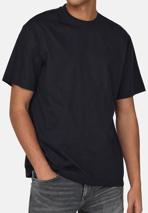 Schwarzes Baumwoll-T-Shirt mit kurzen Ärmeln, rundem Halsausschnitt und lockerer Passform. Geschmeidige Textur; getragen mit grauen Jeans.