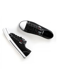 Mustad musta kangast sneakers valge kummist varbata ja tallaga, millel on mustad paelad, kontrastset valget õmblust ning punane aktsentdetail.