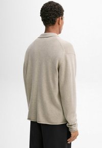 Beige gebreide trui met een kraag, lange mouwen en een iets losvallende pasvorm. Gladde textuur en ribgebreide manchetten en zoom.