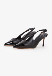 Tacones altos negros tipo slingback con punta afilada, material de cuero, detalle de puntera brillante negra y un delgado tacón de aguja.