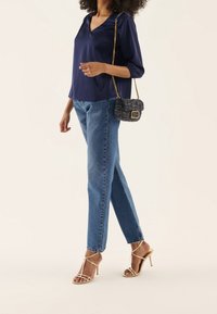 Marinblus i satin med V-ringning, ljusblå högmidjade jeans och beige klacksandaler med remmar. Liten vävd handväska med kedjestropp.