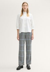 Witte button-up shirt met een hoge kraag, gecombineerd met grijze en blauwe geruite wijde broek. Schoenen zijn zwart met een chunky zool.