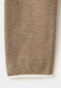 Gros plan d'une manche en tissu tricoté beige avec un bord de poignet blanc, montrant une texture fine et un matériau doux.