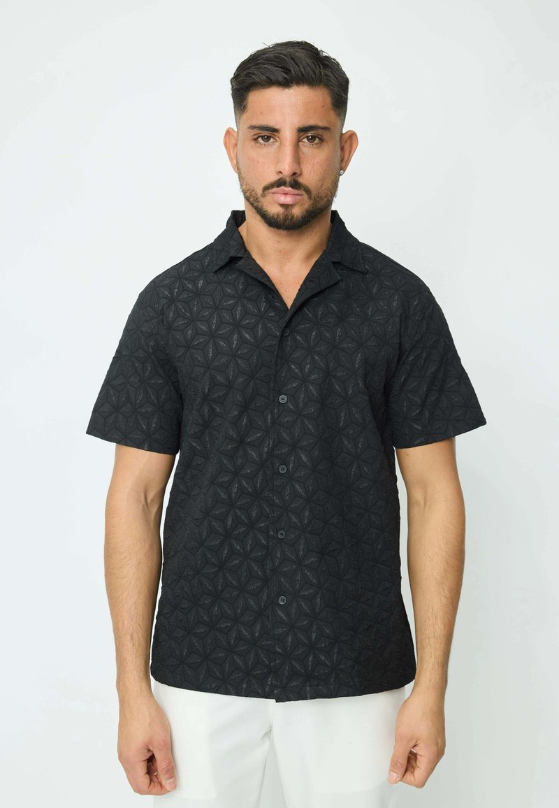 Chemise noire à manches courtes avec texture géométrique et bouton sur le devant. Fabriquée en tissu léger, elle possède un col et une coupe décontractée.