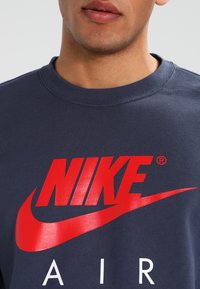 Námořnická modrá mikina s kulatým výstřihem, na přední straně velké červené logo Nike a bílé nápisy "AIR". Materiál z bavlněné směsi.