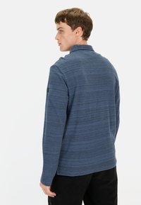 Niebieska, długosleeve bluzka z fakturowanym, paskowanym wzorem, z wysokim kołnierzem i dyskretnym detalem logo na lewym rękawie.