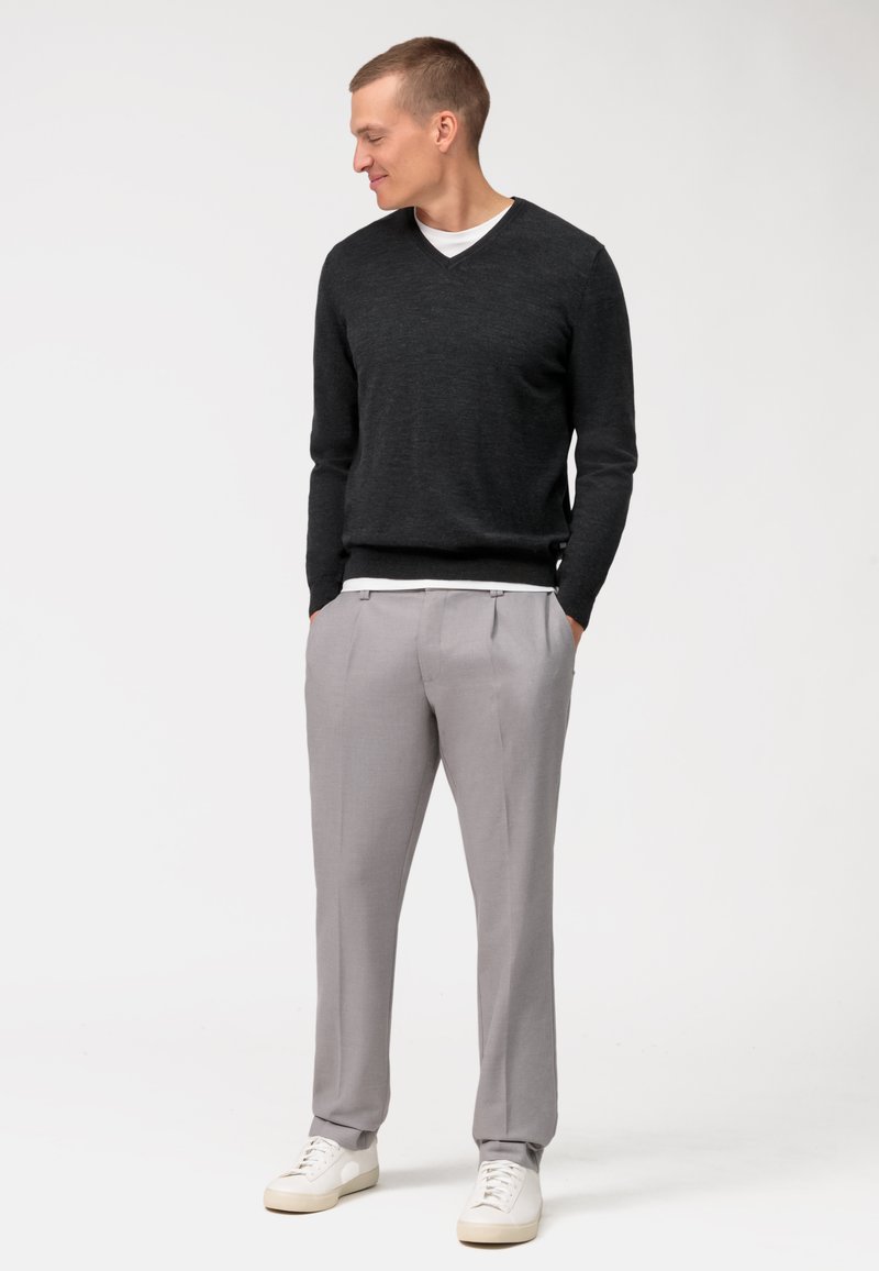 Grijze v-hals trui, lichte knitwear, gecombineerd met lichtgrijze op maat gemaakte broek en witte sneakers. Eenvoudig ontwerp met ribbels aan de mouwen.