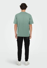 T-shirt en coton vert à manches courtes, col rond et coupe décontractée, associé à un pantalon cargo noir avec poches latérales et poignets ajustés.