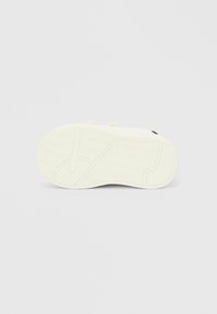 Λευκό πάτο αθλητικού παπουτσιού με σχέδια από ψαροκόκαλο και γραμμικά ανάγλυφα, ορατές πλαϊνές λουρίδες και ανάγλυφο μέγεθος «20» κοντά στη φτέρνα.