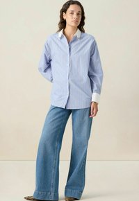 Chemise rayée bleue et blanche avec un col blanc pointu, des manches longues et un devant à boutons, associée à un jean large bleu clair.