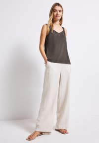 Camisola di raso grigio scuro con bretelle sottili e scollatura a V, abbinata a pantaloni larghi in lino beige chiaro. Sandali piatti completano il look.
