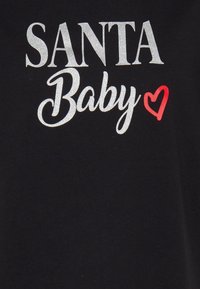 Musta kangas, jossa on sanat "SANTA Baby" hopeanvärisellä kimalletekstillä ja pieni punainen sydän sanan "Baby" vieressä.