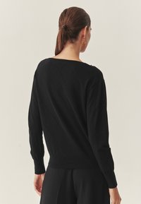 Schwarzer gestrickter Pullover mit einem Rautenmuster, weitem Rundhalsausschnitt und langen Ärmeln. Gerippte Bündchen und Saum. Minimales Design. Weiche Textur.