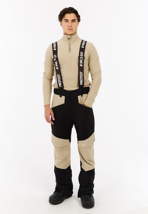 Skikleding met een beige lange mouwen top en twee-kleurige skibroek in zwart en beige met verstelbare bretels en meerdere zakken.
