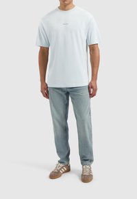 Lichtblauwe katoenen t-shirt met ronde hals en korte mouwen, met de tekst "PURE PATH" in het blauw over de borst. Gemaakt met lichte spijkerbroek.