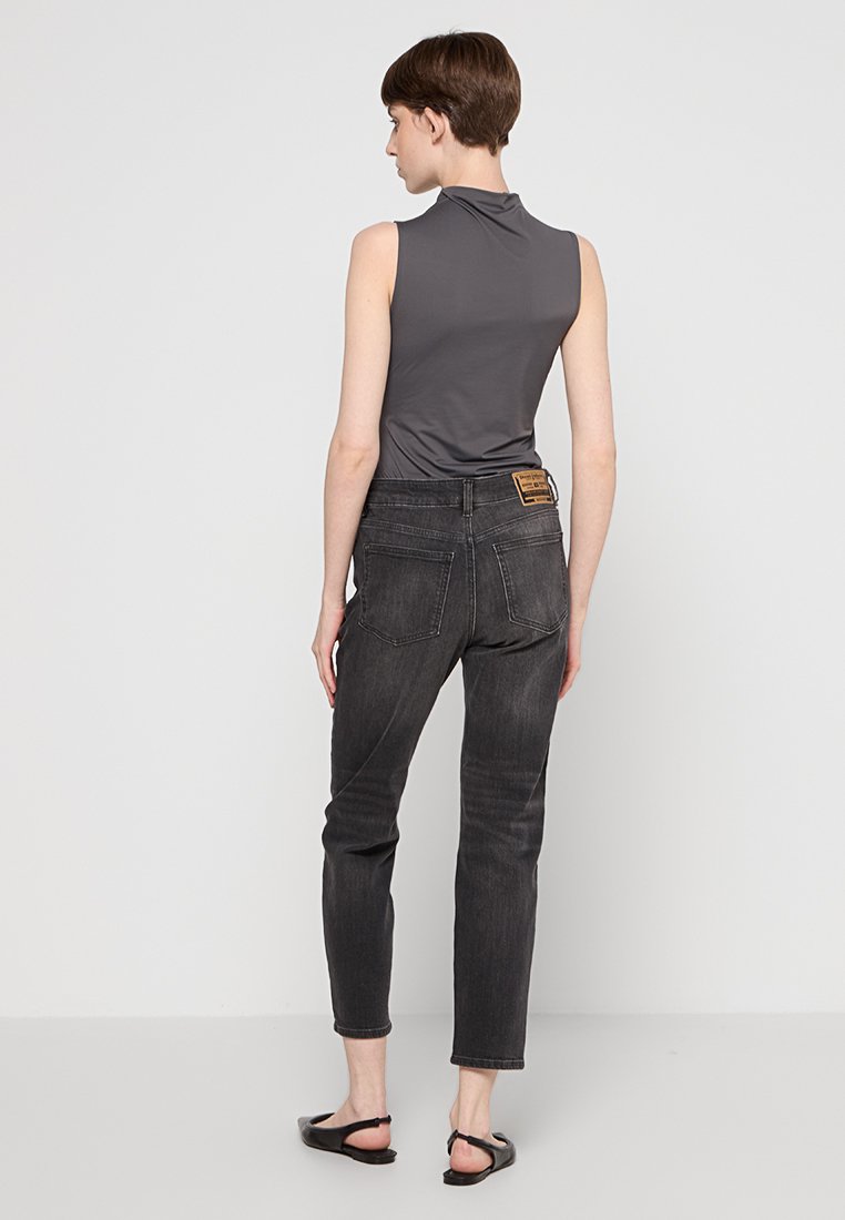Szary bezrękawnik, czarne jeansy z wysokim stanem, obie rzeczy dopasowane. Gładka tekstura, subtelny połysk na bluzce, jeansy mają tylne kieszenie i naszywkę z logo.