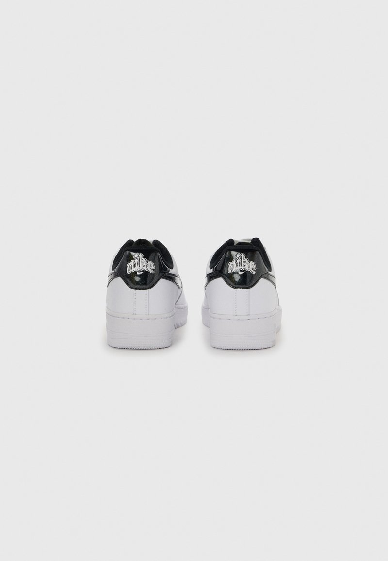 Paire de baskets blanches basses avec des languettes noires au talon ornées du logo "Nike" gothique embossé en argent, vue de dos.