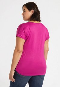 Tætsiddende lyserød t-shirt med korte ærmer, let rundet udskæring, glat tekstur og buet kant, sættet sammen med mørkeblå jeans.