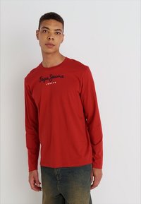 Langærmet rød t-shirt lavet af bomuld, med en rund halsudskæring og sort "Pepe Jeans London" logo tværs over brystet.