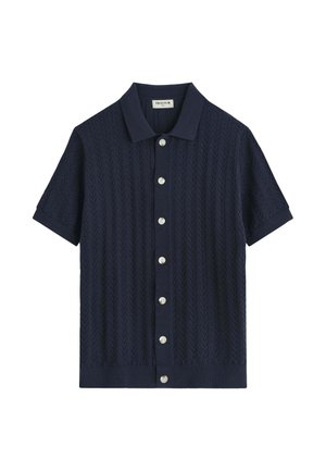 Chemise bleu marine à manches courtes avec motif en maille texturée, col et boutons blancs sur le devant.
