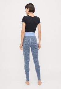 Blå leggings med mönsterdesign, hög midja och ljusblå detaljer. Matchade med en svart åtsittande topp. Minimal textur synlig.