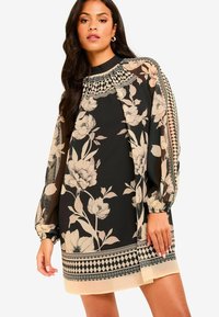 Mustat ja beige kukkakuosiset pitkähihaiset mekko. Ominaisuuksiin kuuluvat korkea kaula-aukko, läpikuultavat hihat ja geomaatiset kuvioinnin yksityiskohdat helman kohdalla.