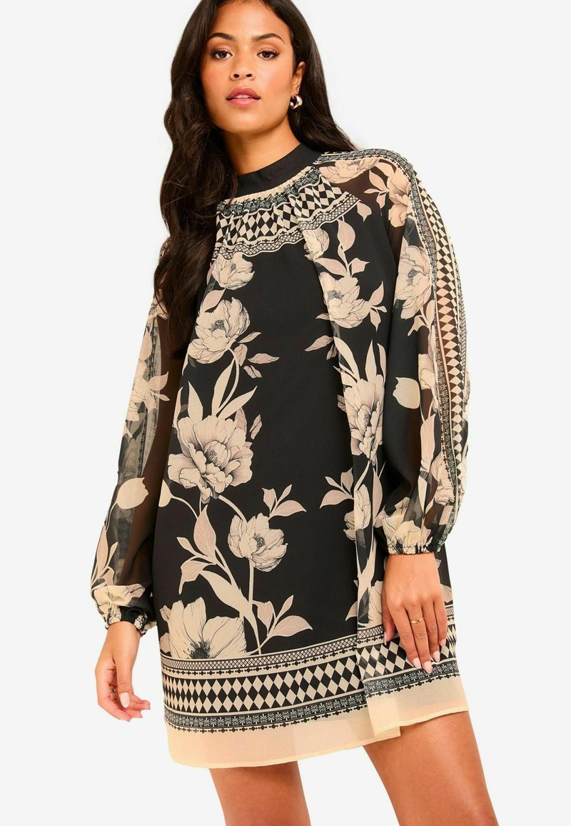 Mustat ja beige kukkakuosiset pitkähihaiset mekko. Ominaisuuksiin kuuluvat korkea kaula-aukko, läpikuultavat hihat ja geomaatiset kuvioinnin yksityiskohdat helman kohdalla.