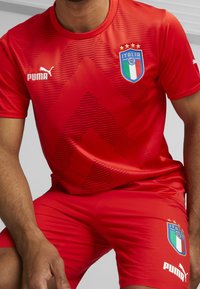 Červený sportovní dres s texturovaným vzorem, s logem Puma a znakem italské národní reprezentace na tričku a trenýrkách.