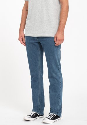 Blue denim jeans with a straight fit, featuring a clean design and visible stitching. Worn with a gray shirt and black sneakers.