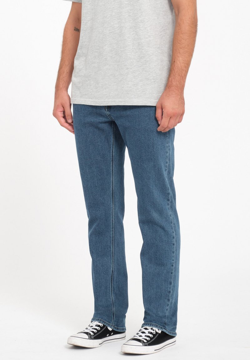 Blue denim jeans with a straight fit, featuring a clean design and visible stitching. Worn with a gray shirt and black sneakers.