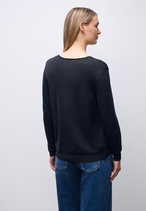 Svart stickad tröja med rundad halsringning och långa ärmar, med en mjuk textur. Kombinerad med blå denimjeans.
