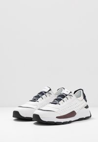 Scarpe sportive bianche con accenti neri, tomaia in pelle textured, punta rotonda e design perforato. Presentano una suola in gomma spessa e lacci con motivo.