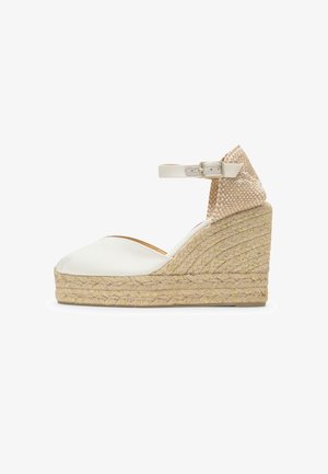 Sandalia cuña blanca con punta cerrada, plataforma trenzada de yute, tira en el tobillo con hebilla y contrafuerte en el talón beige con estampado.