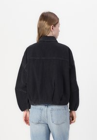 Giacca di jeans nera con una vestibilità comoda, colletto ripiegato e maniche lunghe, caratterizzata da una cucitura sulla schiena e una consistenza morbida.