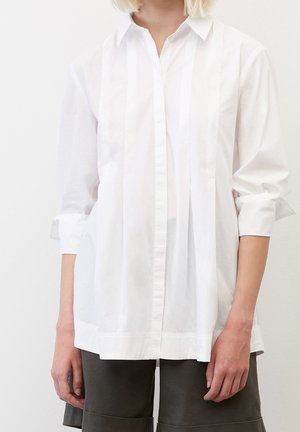 Chemise blanche à manches longues et boutonnières avec des rayures verticales, un col classique et des poignets retroussés, fabriquée en tissu léger.