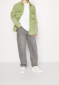 Camisa de pana verde con dos bolsillos en el pecho, combinada con vaqueros de pierna ancha grises y zapatillas blancas, con una textura suave y un corte relajado.