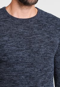 Mörkblått stickat tröja med ett strukturerat mönster, rund halsringning och ribbade ärmslut. Tyget ser mjukt och elastiskt ut.