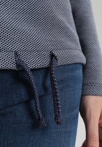 Top leggero e strutturato con un motivo geometrico navy, caratterizzato da un orlo con coulisse e una vestibilità comoda, abbinato a pantaloni in denim scuro.