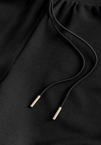 Tela negra con un cordón negro que tiene terminales cilíndricos metálicos dorados en una cinturilla fruncida.