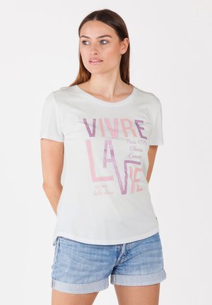 T-shirt gris clair à manches courtes avec un col rond, ornée de texte rose et pailleté. Assortie à un short en jean, affichant une coupe décontractée.