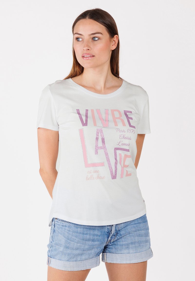 Camiseta de manga corta gris claro con cuello redondo, con texto en rosa y brillante. Combinada con pantalones cortos de mezclilla, que muestran un ajuste relajado.