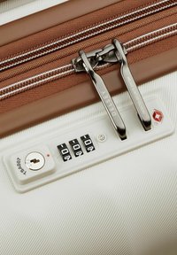 Witte gestructureerde koffer met een bruine rits en een ingebouwd TSA-goedgekeurd slot met een sleutelgat en cijfersloten.