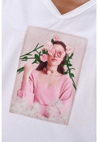 Witte T-shirt met een vierkant, geborduurd bloemenpatroon met een pastelkleurig roze portret en bloemaccenten, waaronder rozen en bladeren.