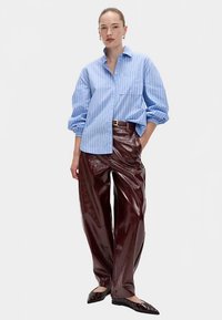 Blåstribet skjorte med knapper og lange ærmer, kombineret med blanke, bordeaux brede bukser. Sorte spidse flade sko med udskæringsdetaljer.