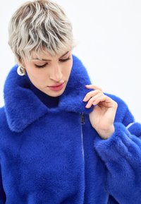 Cappotto in pelliccia sintetica blu con ampio colletto, chiusura con zip e texture morbida. Presenta una vestibilità comoda e maniche morbide.