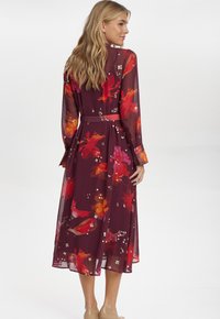 Lång, genomskinlig bordeauxklänning med livfulla blommönster i rött, orange och vitt, med ett matchande bälte och knäppte manschetter.