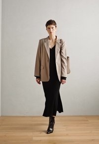 Béžový oversize blazer přes černé šaty, doplněný lesklými černými kotníkovými botami. Jednoduchý design s čistými liniemi a minimálním zdobením.