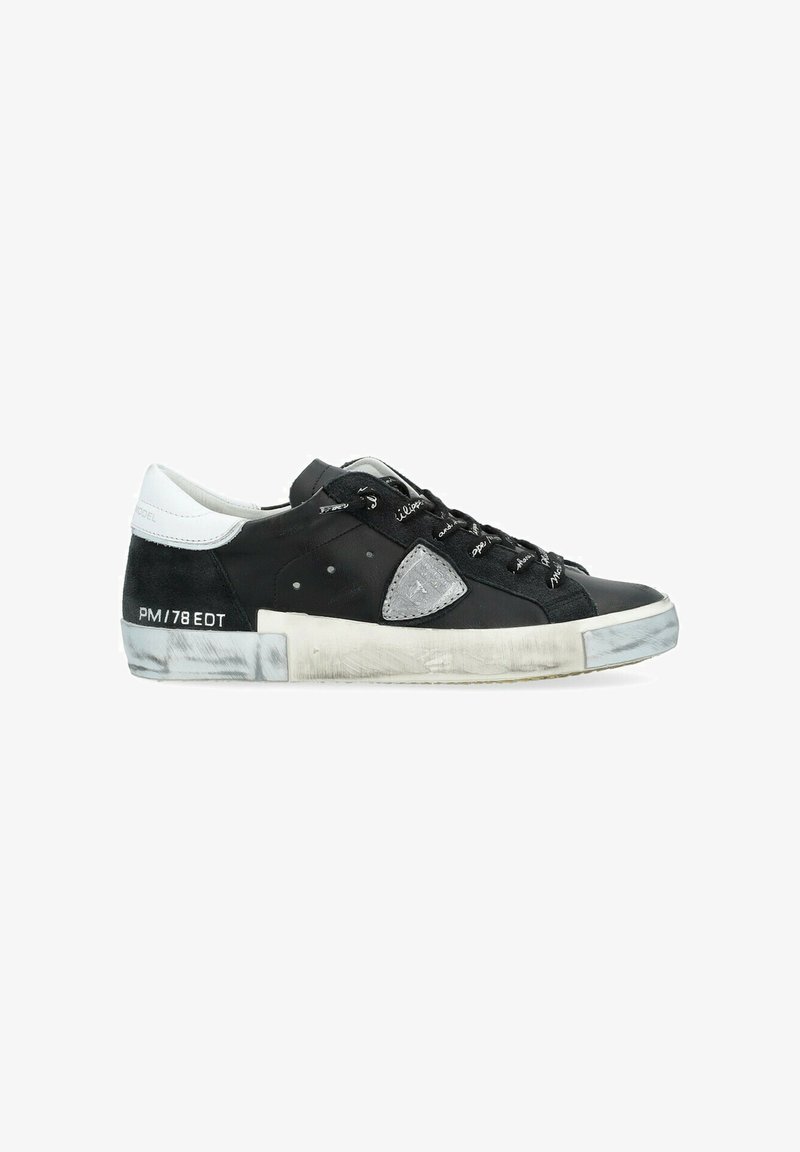 Sneaker bianco e nero con tomaia in suede e pelle, un accento triangolare grigio notevole e suola marmorizzata sbiadita. Presenta lacci decorativi.