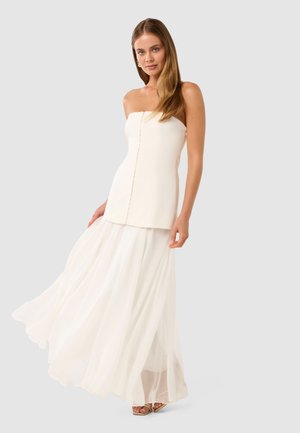 Strapless hvit kjole med en tettsittende overdel og en flytende, lagdelt skjørt. Laget av lett stoff, med detaljert knapp foran.