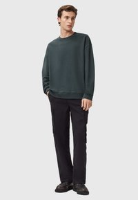 Felpa verde scuro con vestibilità normale, scollatura rotonda e polsini a costine, abbinata a pantaloni cargo neri con tasche laterali e gamba dritta.